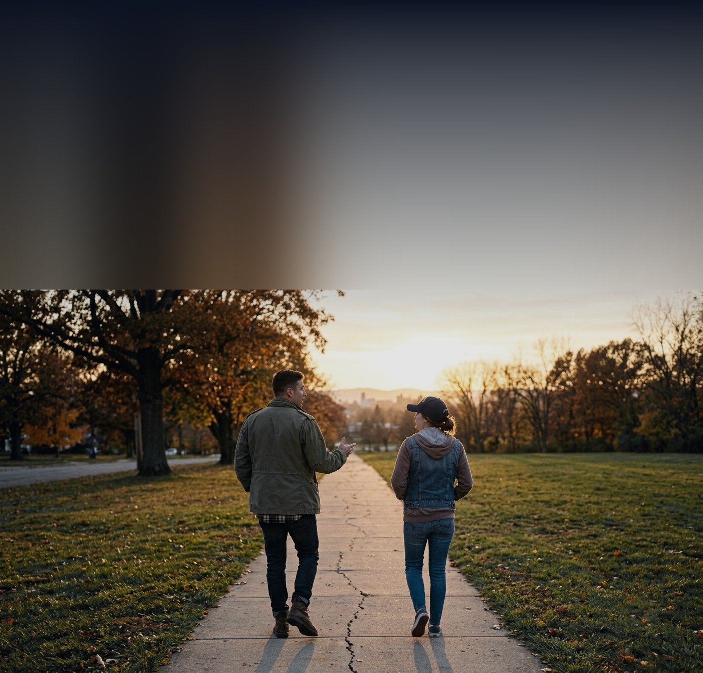Two veterans walking side by side along a park path at sunset, talking.